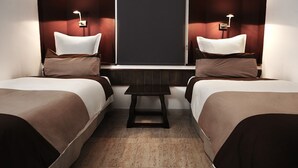 A hotel room with two single beds, a small table, and a dark headboard.