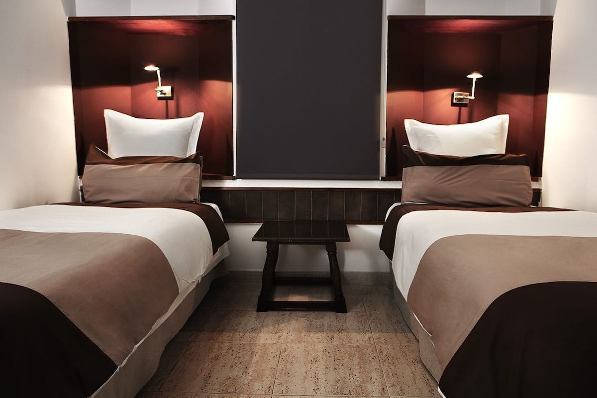 Ein Hotelzimmer mit zwei Einzelbetten, einem kleinen Tisch und einem dunklen Kopfteil.