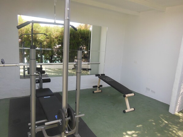 Un gimnasio con banco, estante para pesas y espejos.