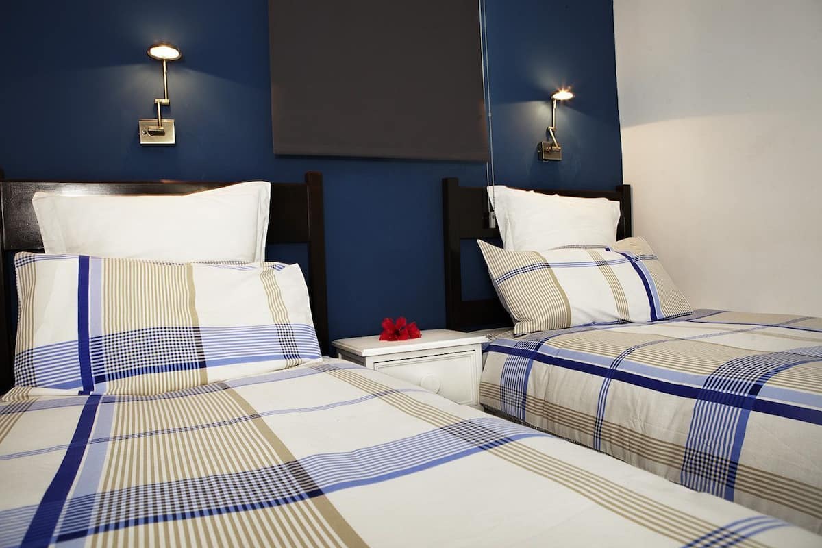 Ein Hotelzimmer mit zwei Betten, jeweils mit einer gestreiften Tagesdecke, einem Nachttisch mit Lampe und einem an der Wand montierten Fernseher.
