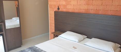 A hotel room with a brick-patterned wall, a wooden headboard, a bed with white bedding, a small wooden nightstand, and a mirror.