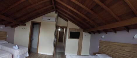 A room with two beds, wooden beams on the ceiling, and a hallway leading to another room.