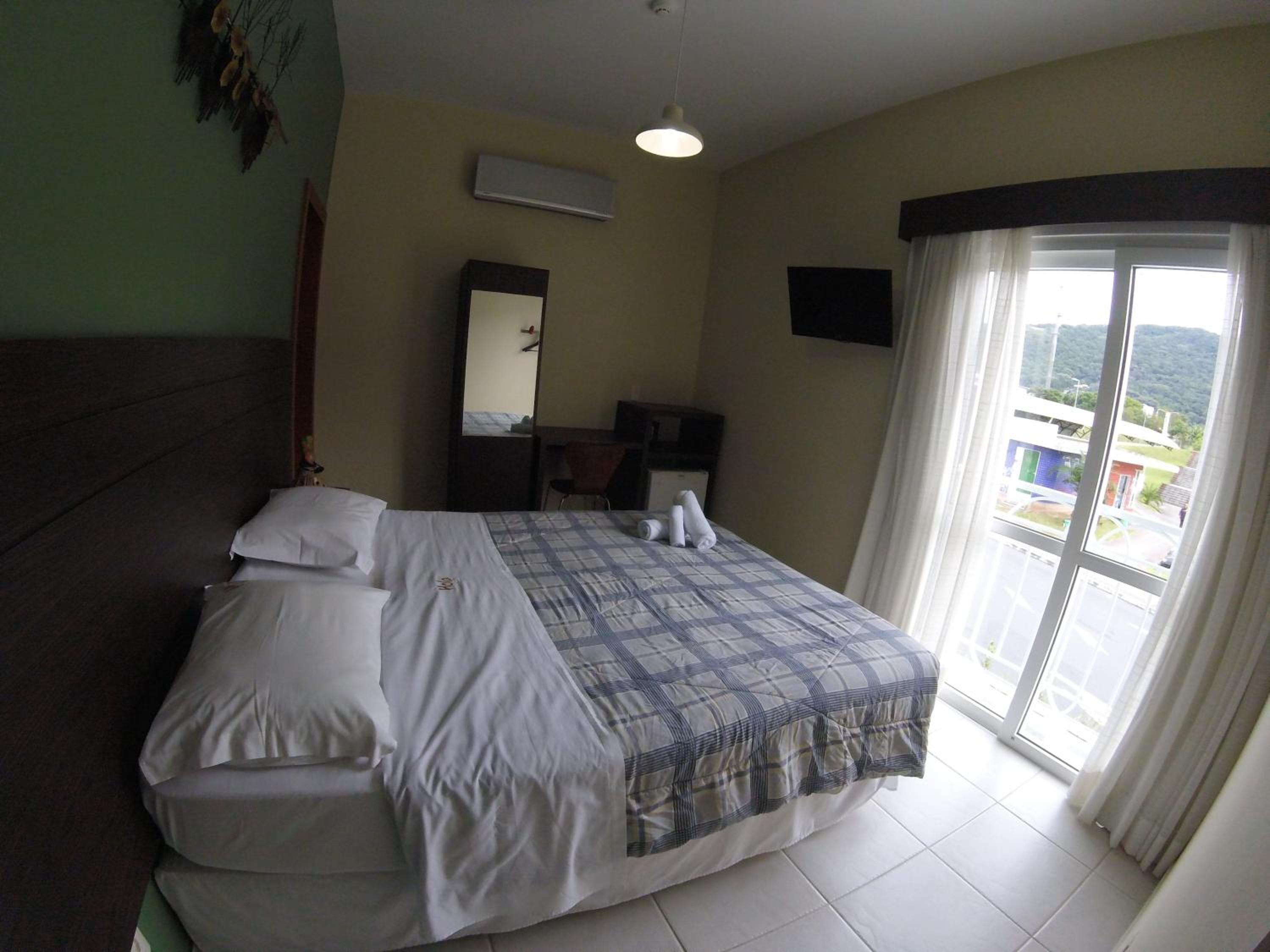 A hotel room with a bed, a desk, a chair, a mirror, and a window with a view.