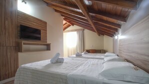 A hotel room with wooden beams, a TV mounted on the wall, and neatly made beds with towels. - Hotel Hola (Florianópolis)