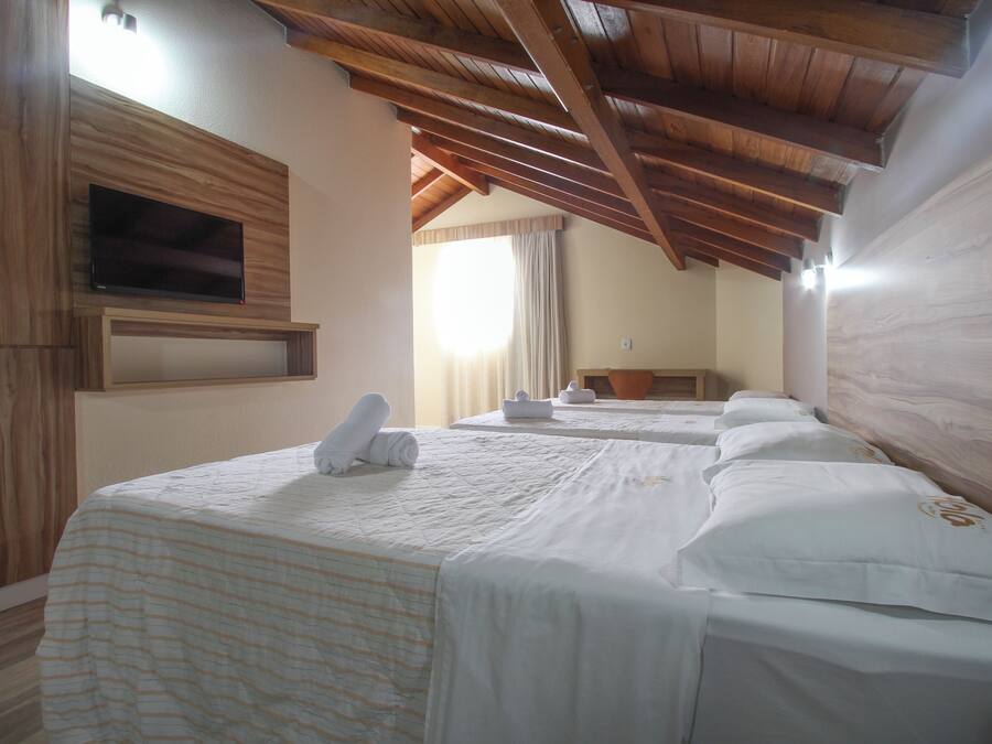 Habitación de hotel con vigas de madera, un televisor montado en la pared y camas ordenadas con toallas.