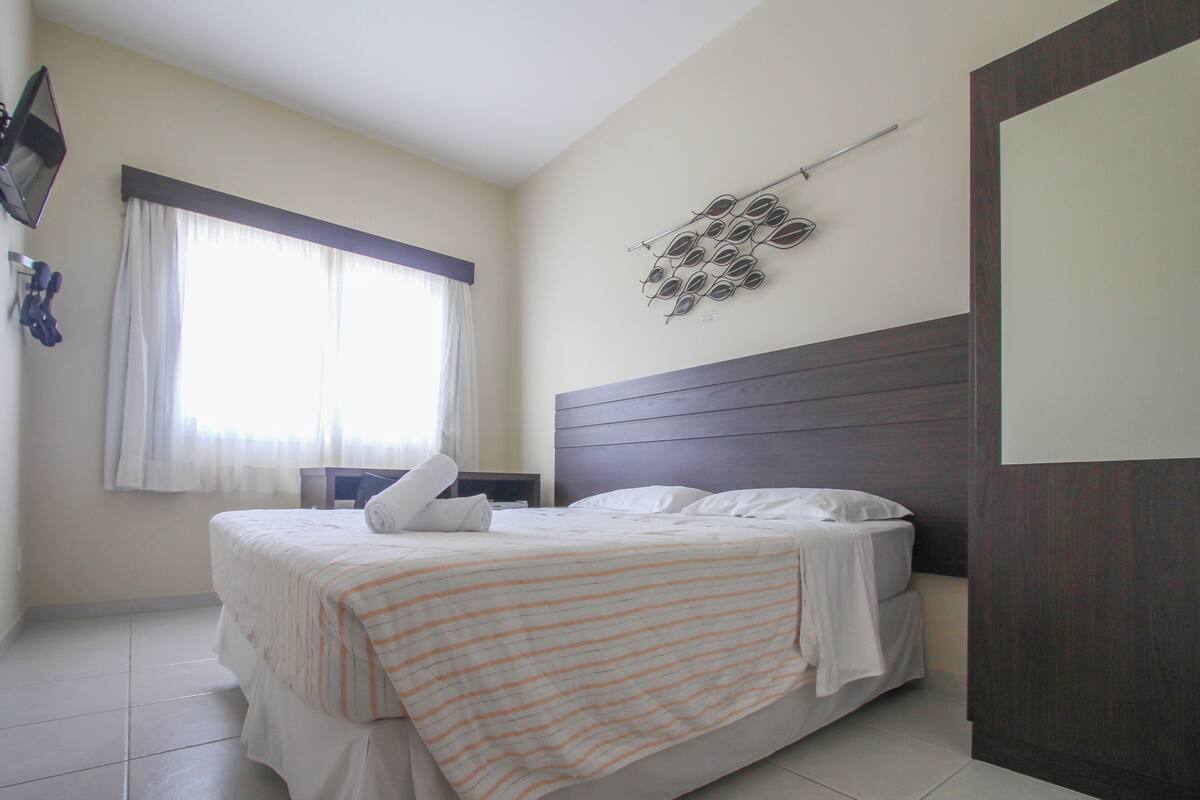 A hotel room with a bed, a window with curtains, a wall-mounted decoration, and a door.