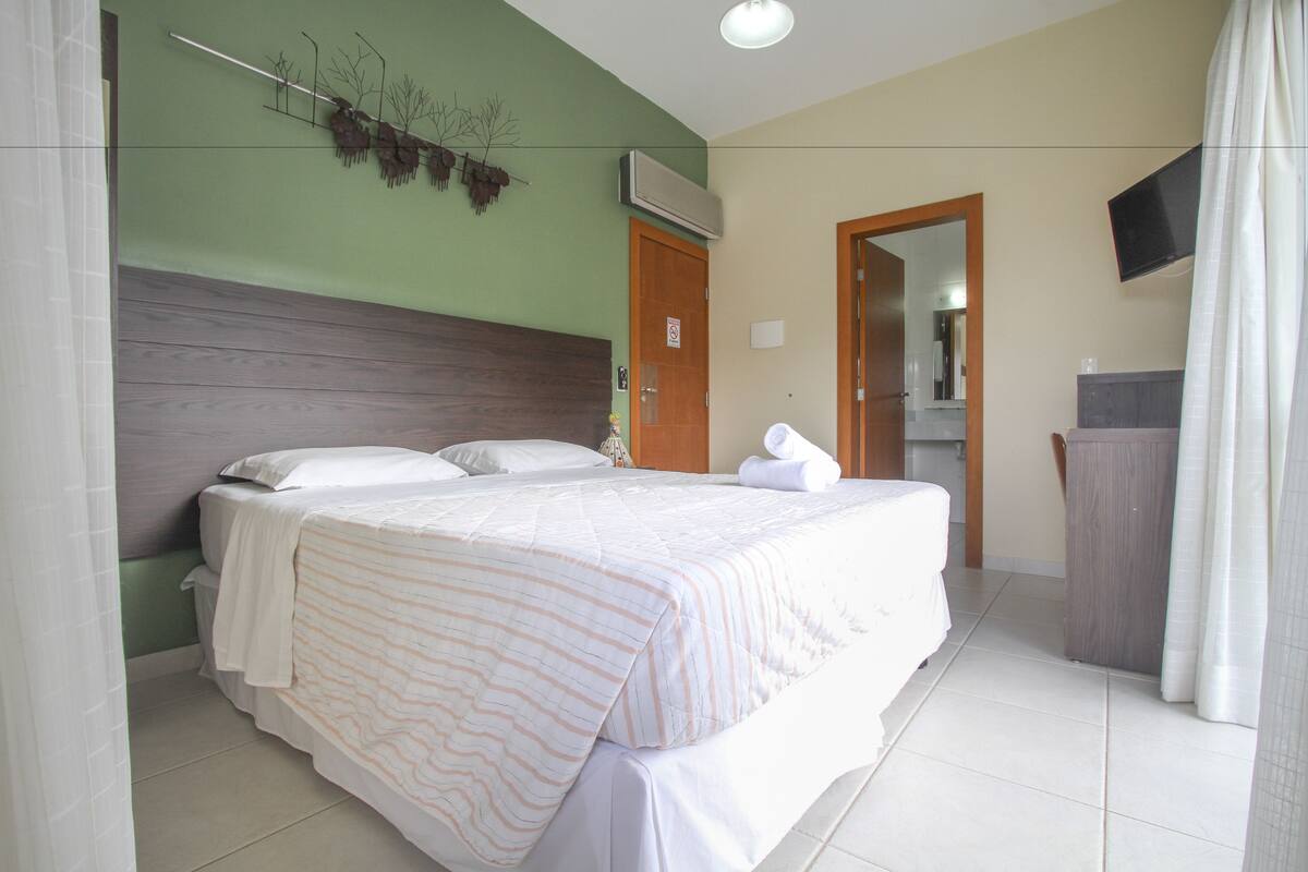 A hotel room with a large bed, a wooden headboard, a flat-screen TV mounted on the wall, and a wooden wardrobe.