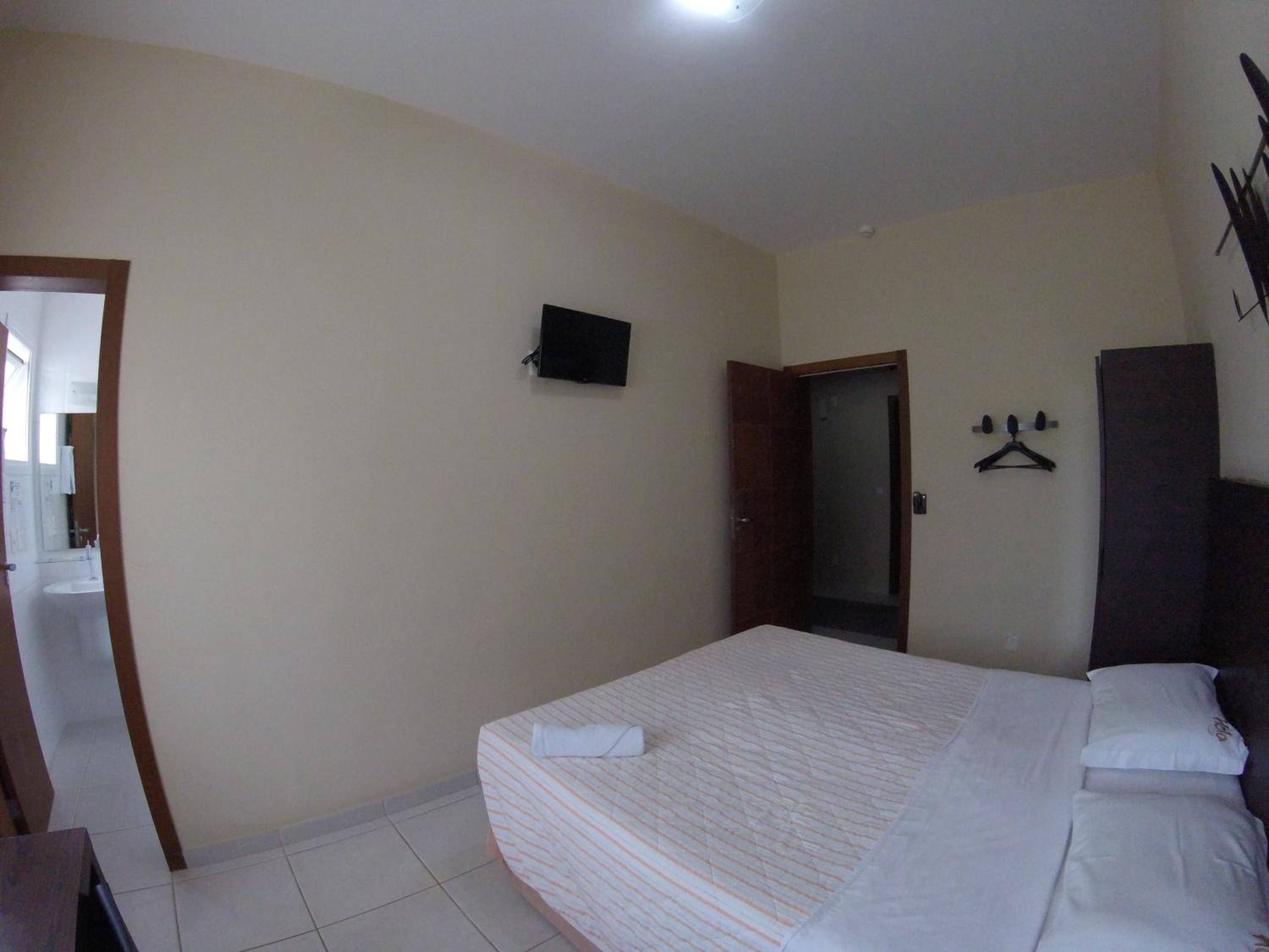 A bedroom with a bed, a TV, a wardrobe, and a door leading to another room.