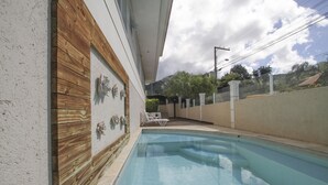 A swimming pool with a wooden deck and a white wall with decorative elements. - Hotel Hola (Florianópolis)