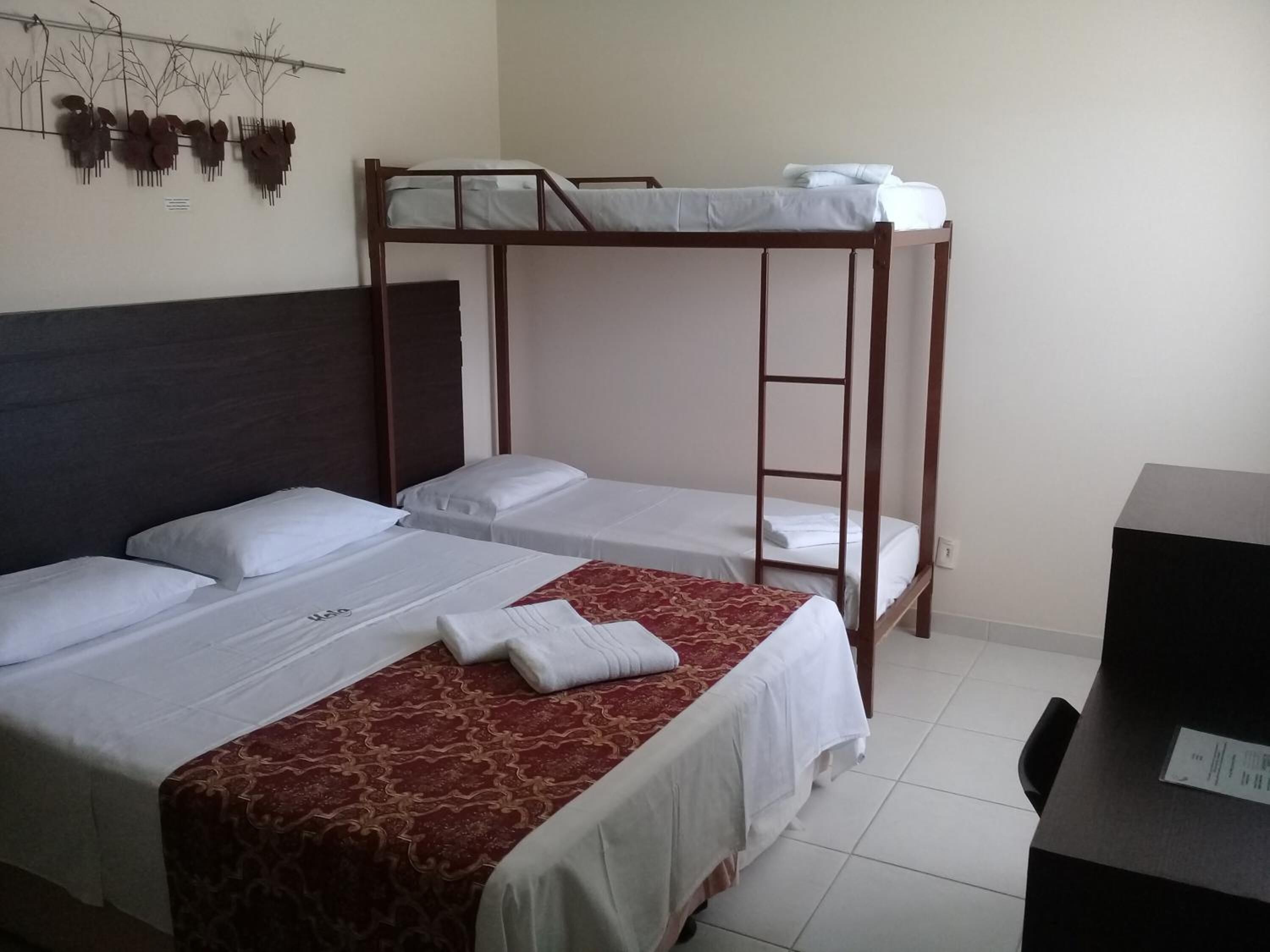 A hotel room with a bunk bed, two single beds, a desk, and a wall-mounted artwork.