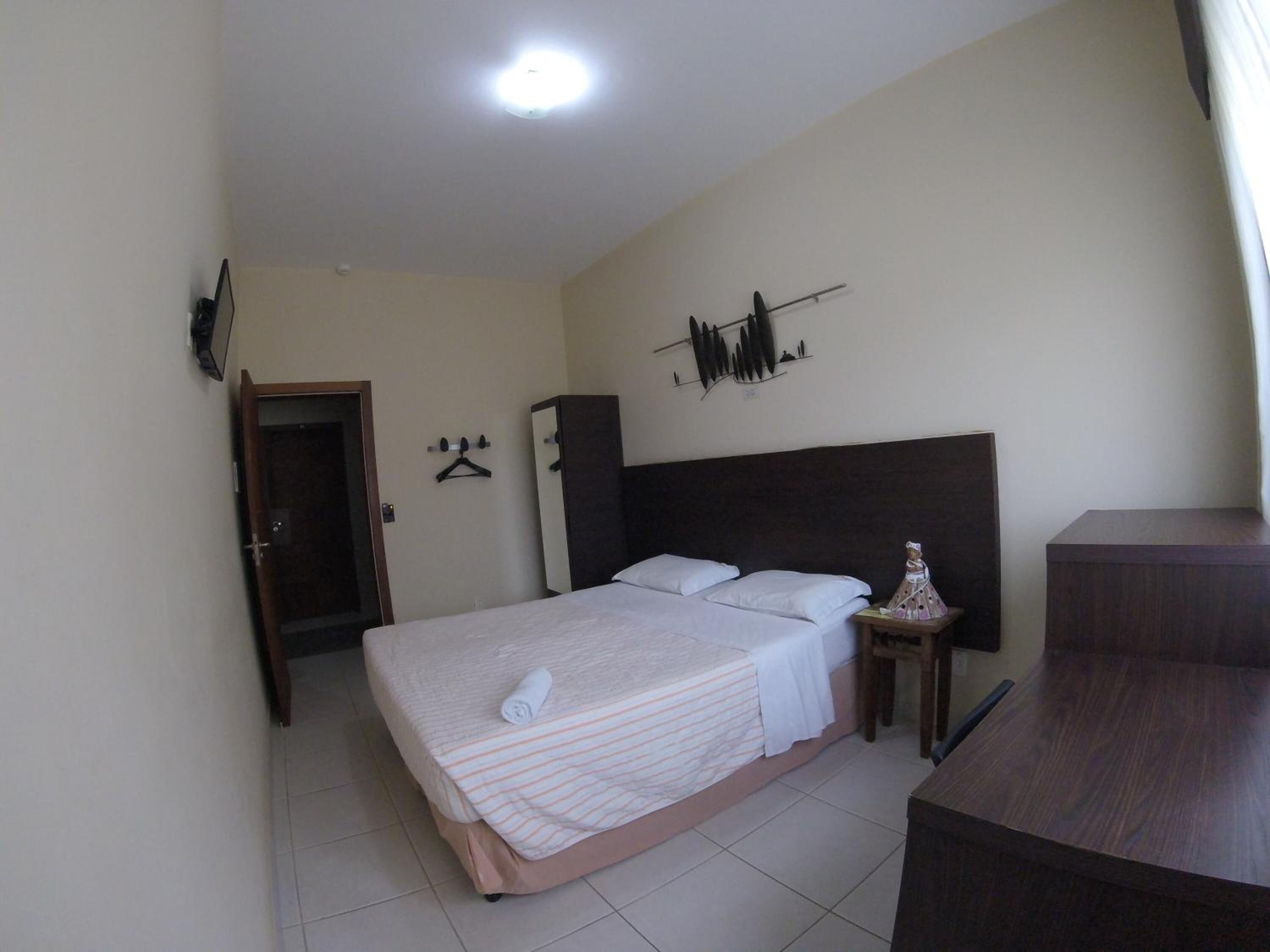 Un dormitorio con cama, armario, escritorio y estante fijado a la pared.