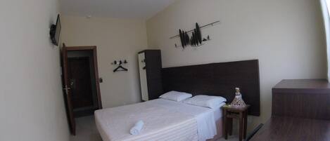 Un dormitorio con cama, armario, escritorio y estante fijado a la pared.