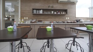 A modern kitchen with wooden cabinets, a countertop with various kitchen items, and a dining area with tables and chairs. - Hotel Hola (Florianópolis)