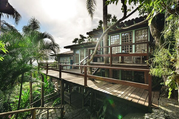 A traditional wooden building with multiple levels, connected by wooden walkways, surrounded by lush tropical vegetation.