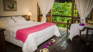 A bedroom with a bed, a nightstand, a table with a chair, and a window with curtains. - Porto Pousada Saco da Capela (Ilhabela)