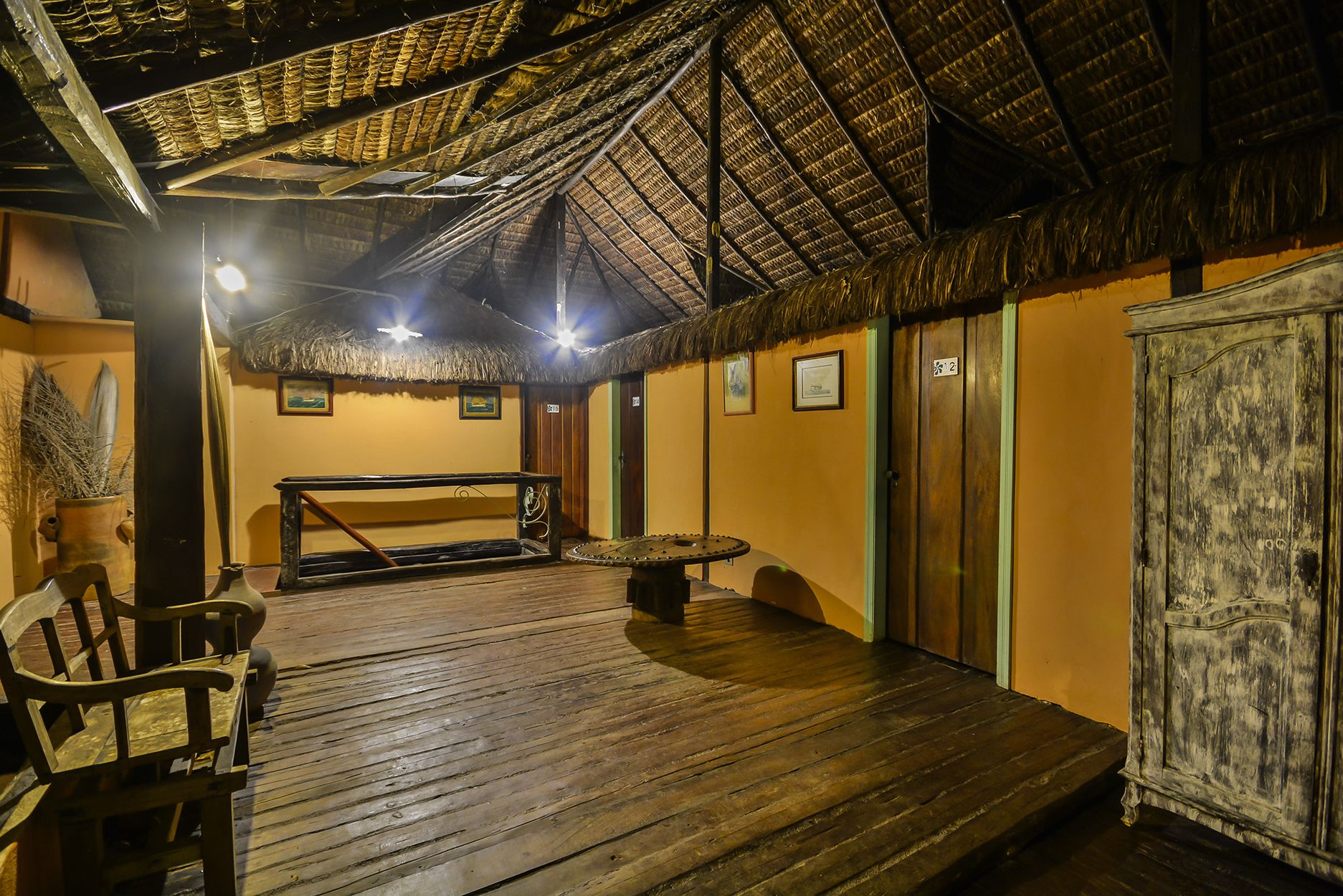 A wooden deck with a thatched roof, a table, chairs, and a cabinet.