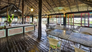 A spacious indoor area with a thatched roof, wooden flooring, and multiple tables and chairs. - Porto Pousada Saco da Capela (Ilhabela)