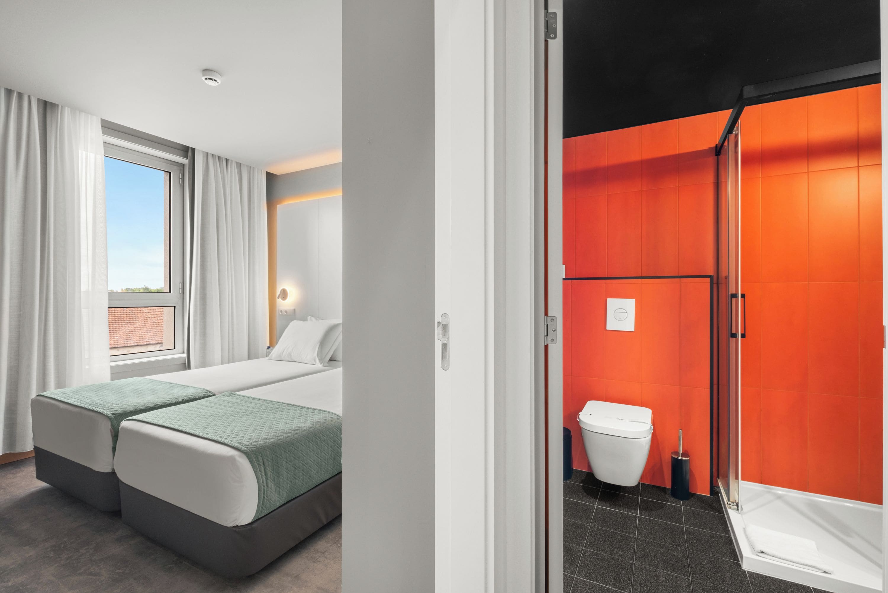 Habitación de hotel con cama, mesita de noche, ventana con cortinas y vistas al exterior.