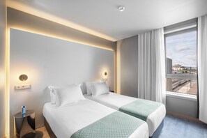 A hotel room with two beds, a bedside table, a nightstand, a window with curtains, and a view of the outside. - Basic Braga by Axis (Braga)