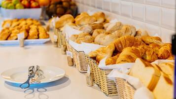 Buffet com diversos pães e doces, incluindo croissants e baguetes, dispostos em cestas.