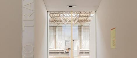 A hallway with a glass door leading to a room with a metal framework ceiling.