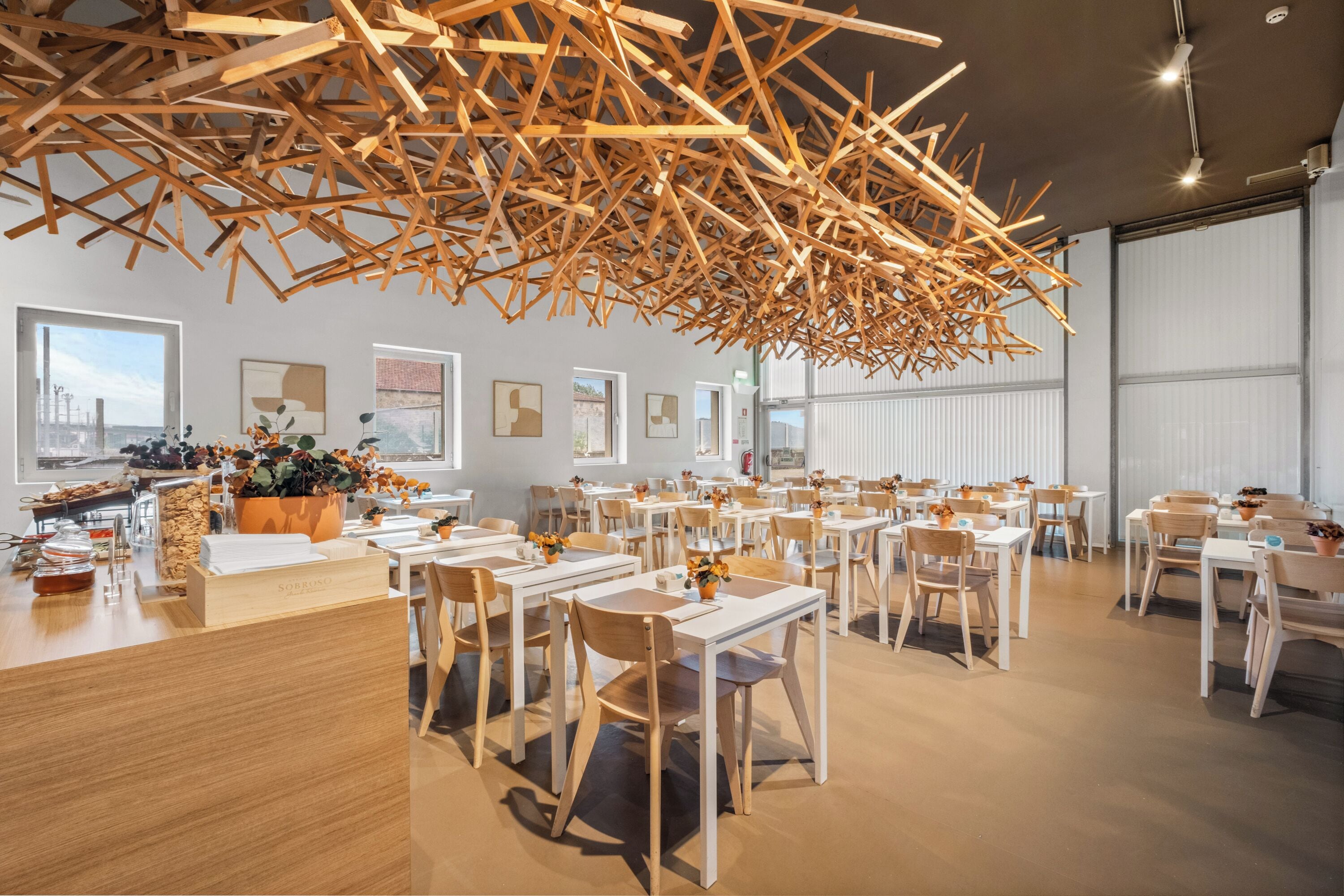 A modern dining area with wooden tables and chairs, a ceiling with wooden beams, and city views through large windows.