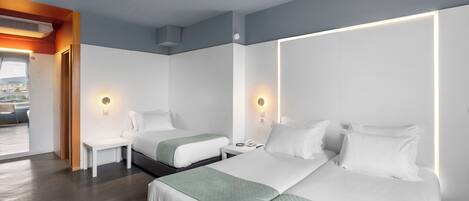 Una habitación de hotel moderna con dos camas, una mesita, lámparas de noche y vistas al exterior.