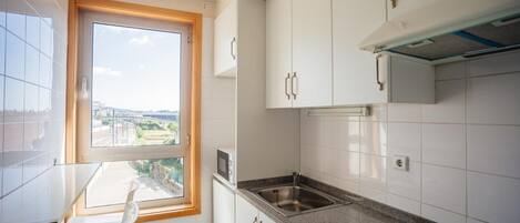 Una cocina con armarios blancos, un lavamanos de acero inoxidable y una ventana con vistas a la ciudad.