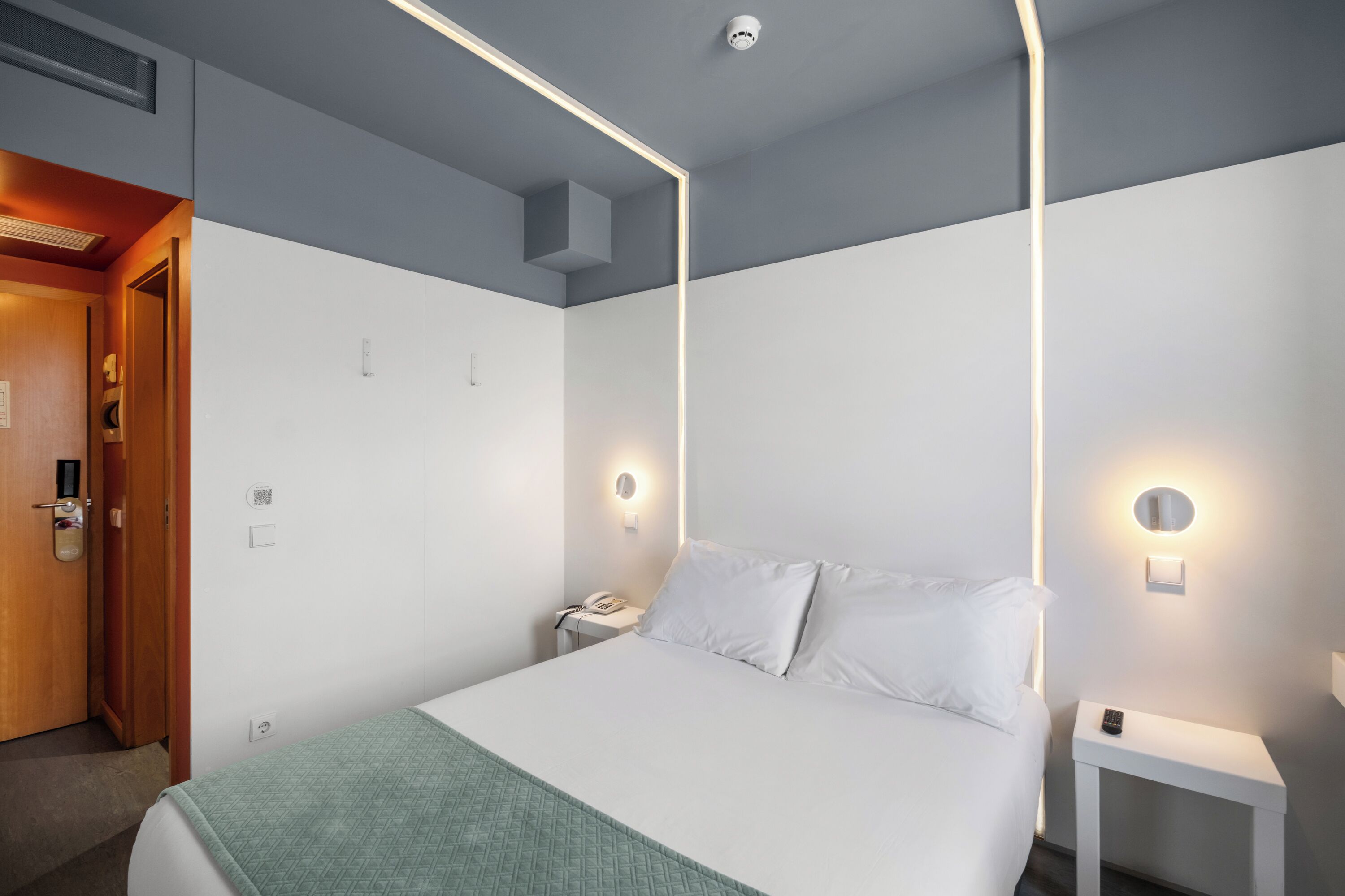 A hotel room with a bed, bedside tables, a nightstand, a phone, and a door.