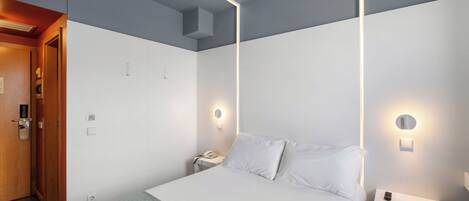 A hotel room with a bed, bedside tables, a nightstand, a phone, and a door.