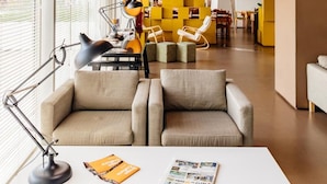 Un interior modern amb un escriptori blanc, una làmpada i una revista. Al fons, hi ha dos sofàs beix i una biblioteca groga.