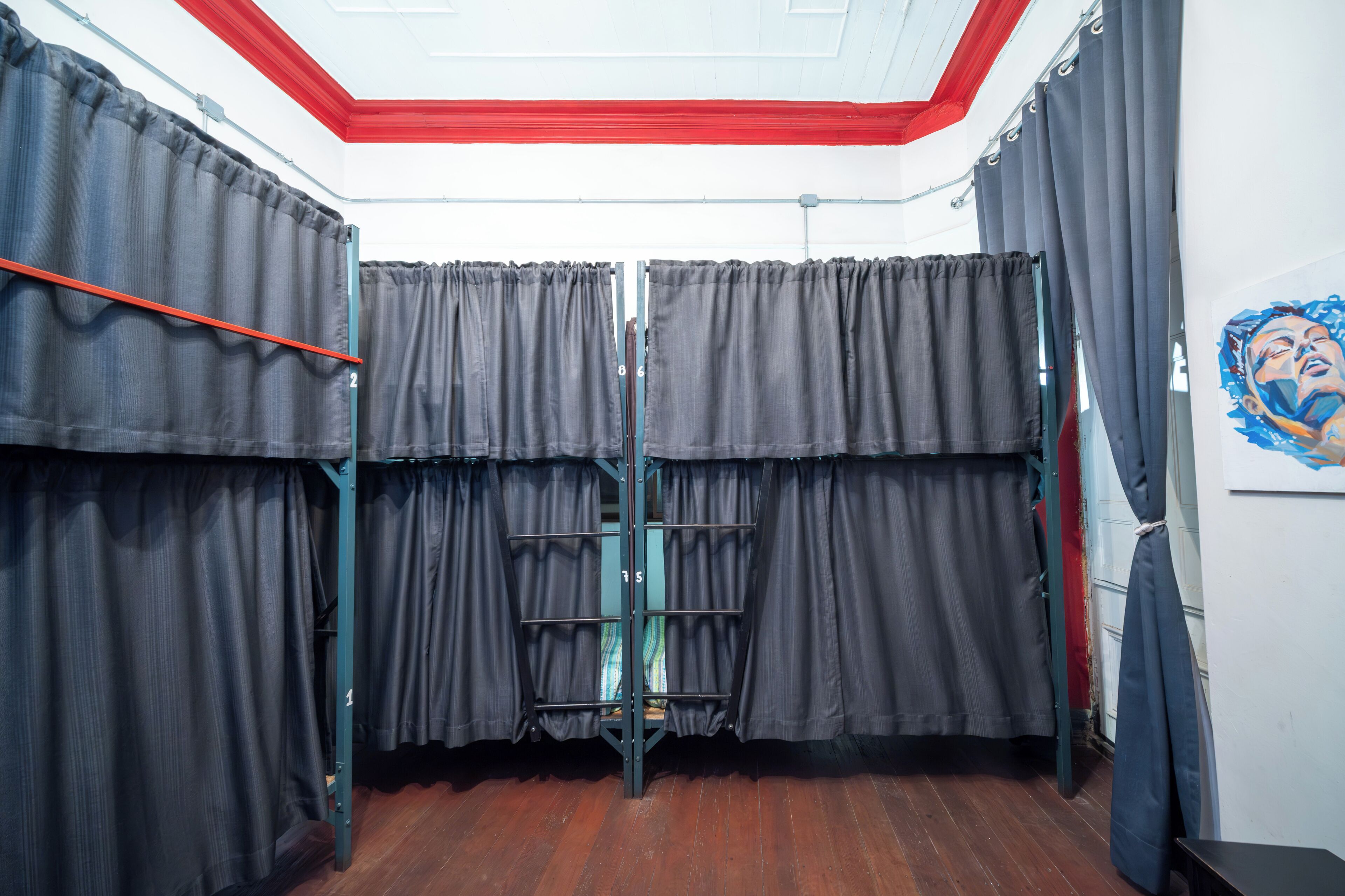 Une chambre avec un lit superposé, des rideaux gris, un plafond rouge et un tableau accroché au mur.