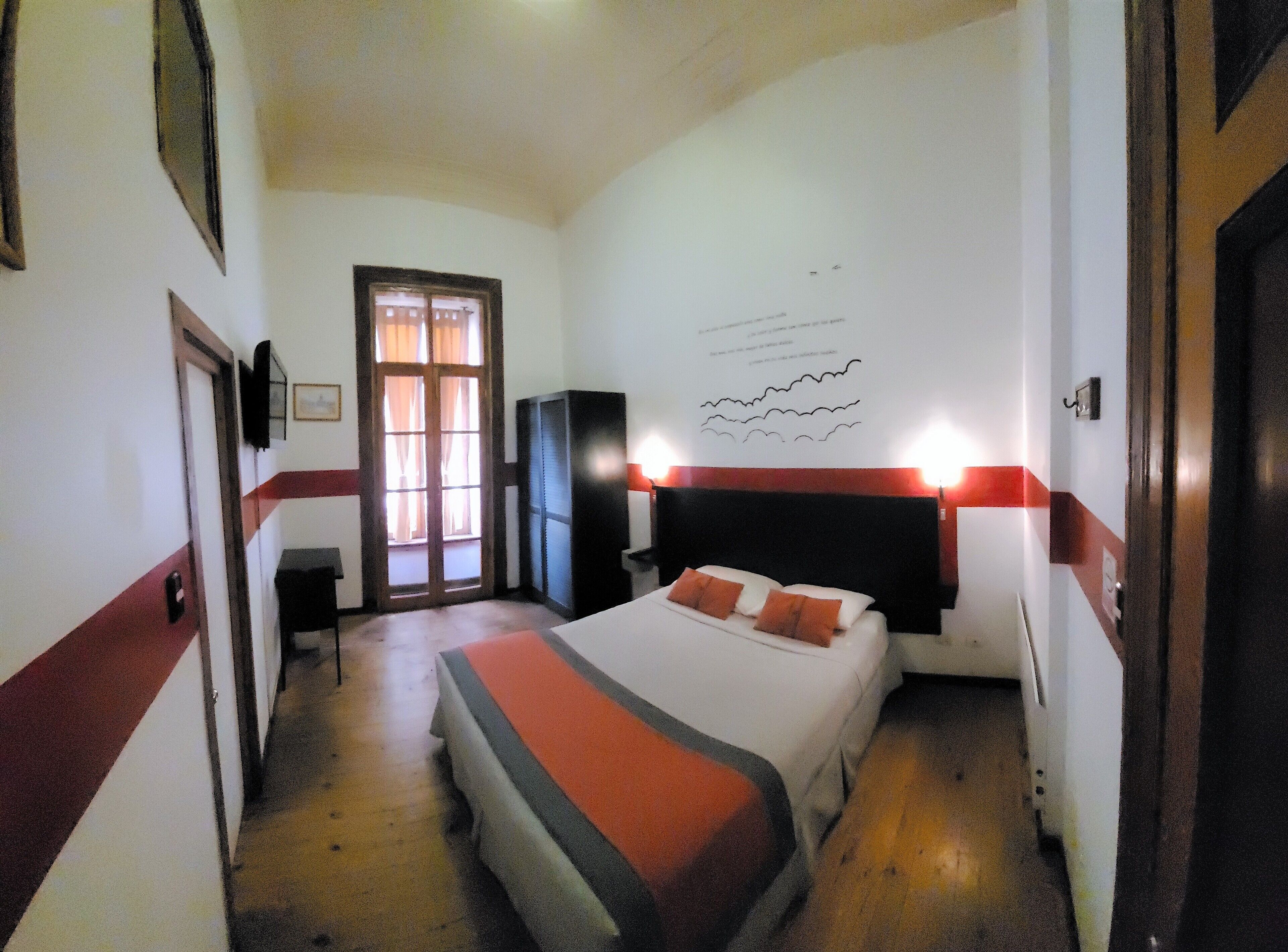 Ein Hotelzimmer mit Bett, Schreibtisch, Kleiderschrank und einem fensterbepflanzten Fenster.