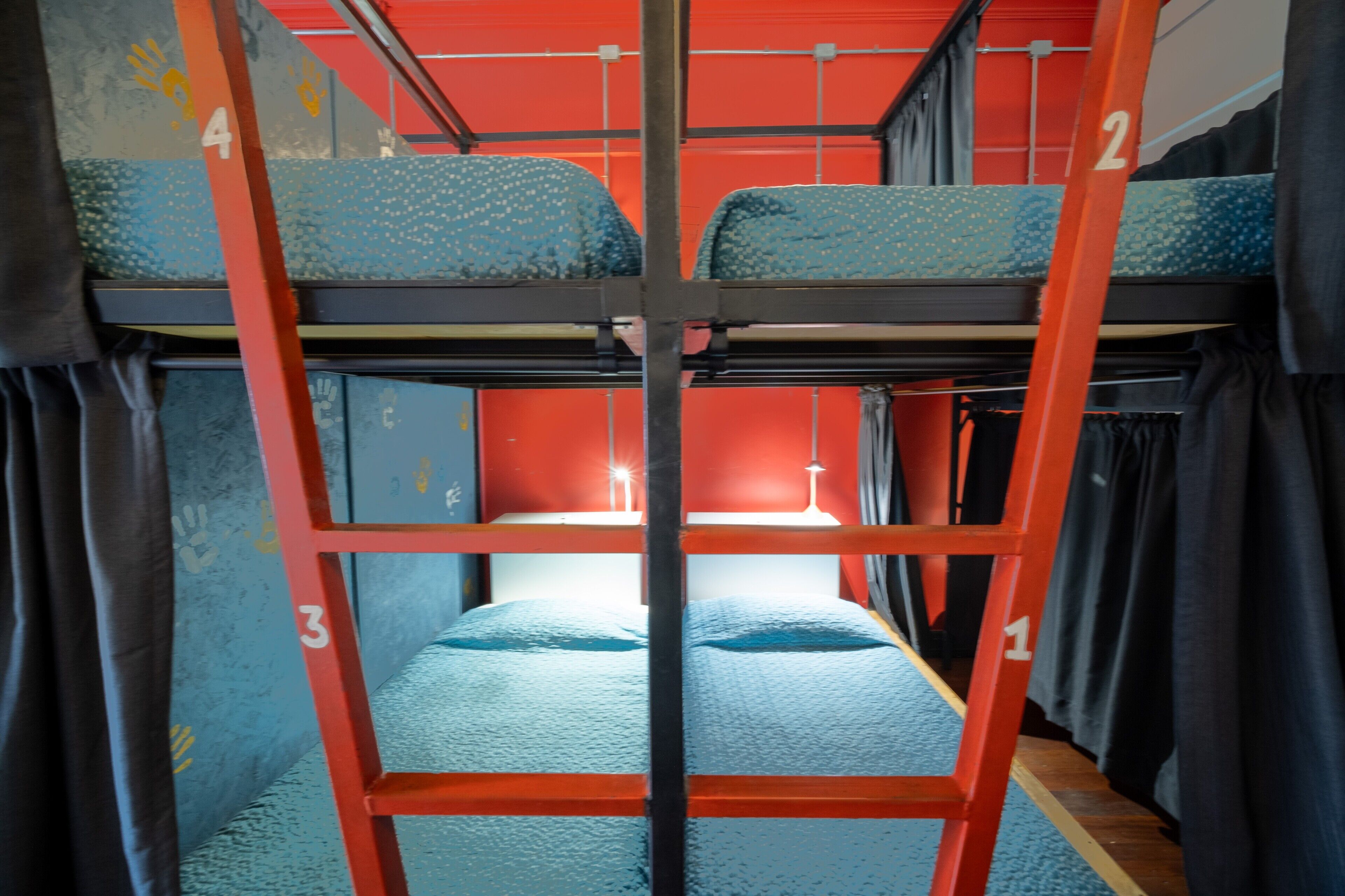 A bunk bed with four levels, numbered 1 to 4, in a room with red walls and curtains.