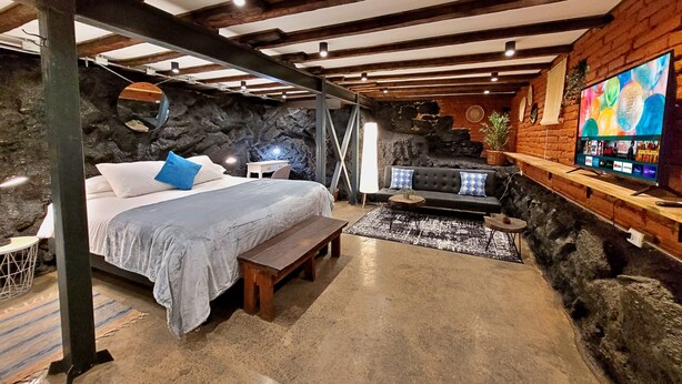 Un dormitorio con cama, un banco, un sofá, un televisor y una pared de piedra.