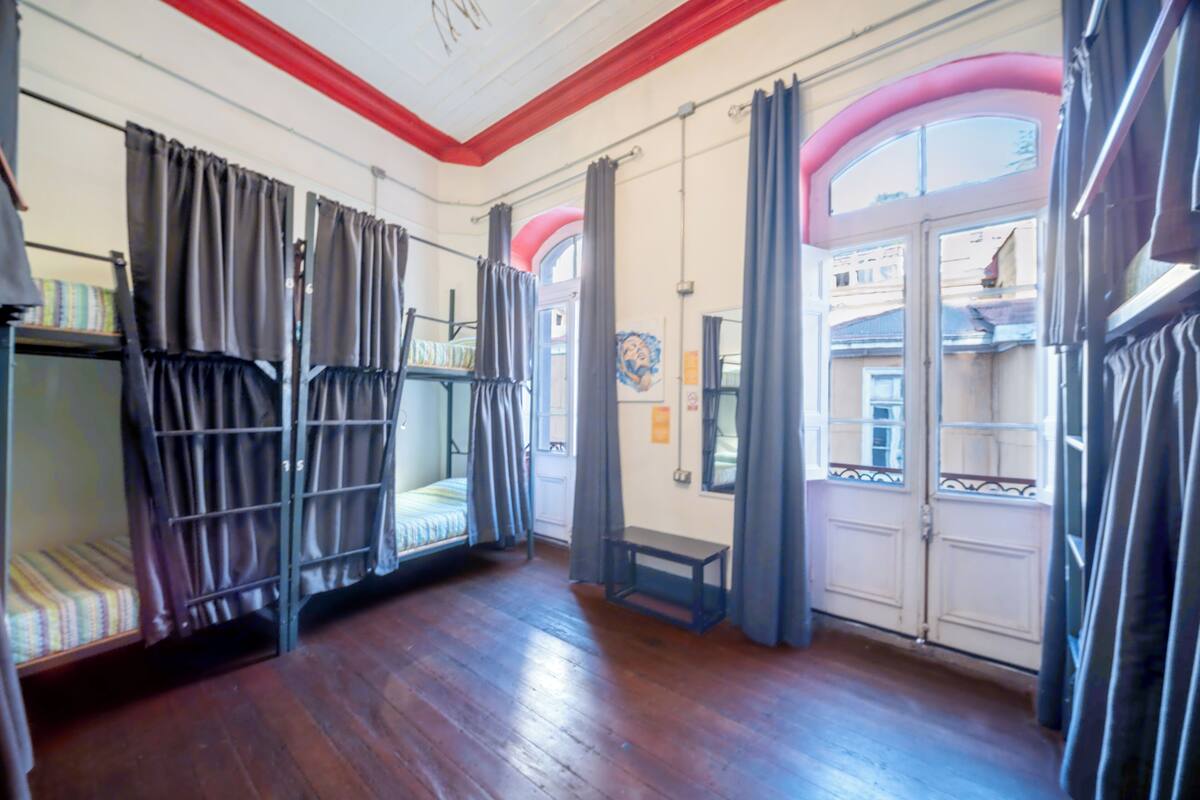 Quarto com beliches, um banco e uma porta que dá para uma varanda externa.