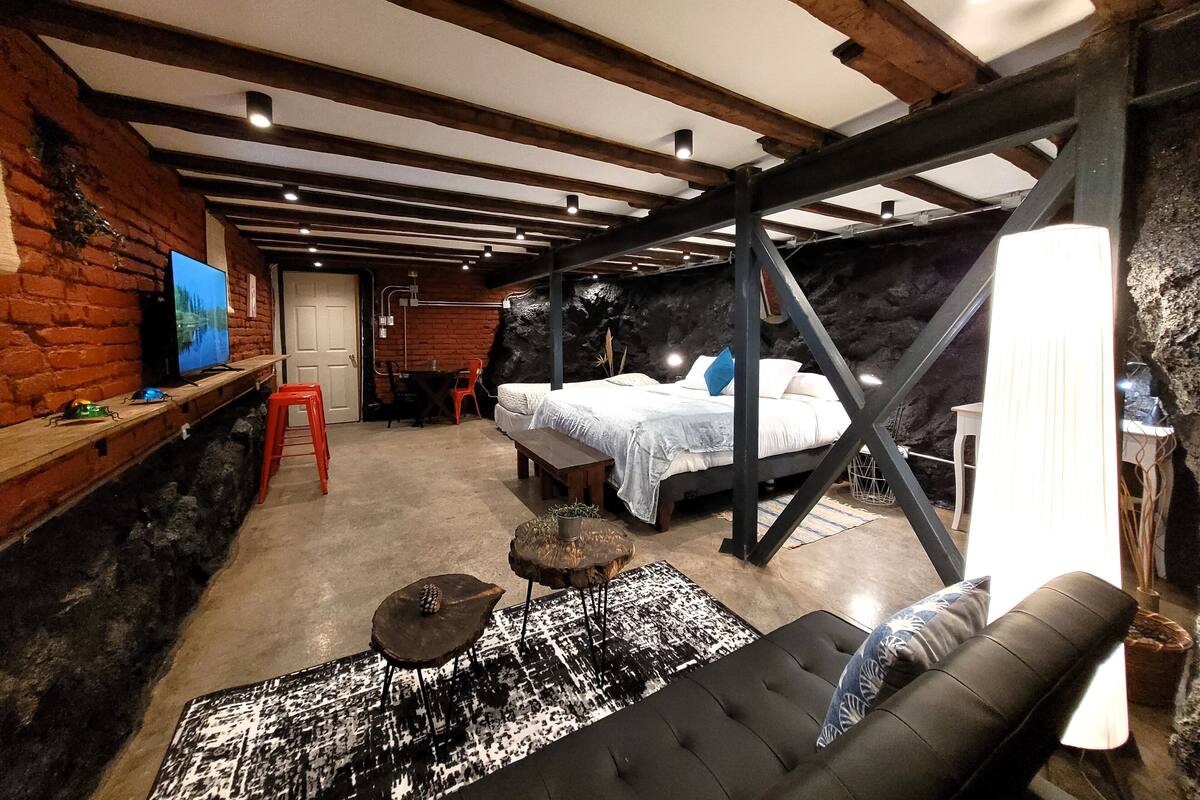 Quarto rústico com vigas aparentes, uma cama, uma escrivaninha e uma televisão.