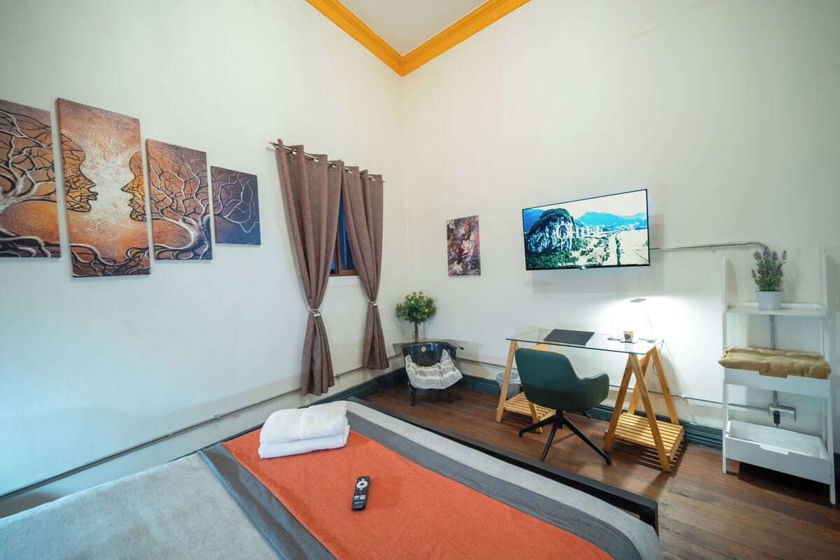 Quarto com cama, escrivaninha, cadeira, televisão e obras de arte nas paredes.