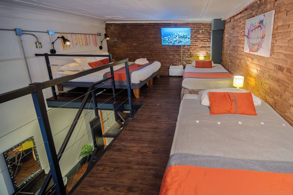 Quarto com beliches, televisão e parede de tijolos.