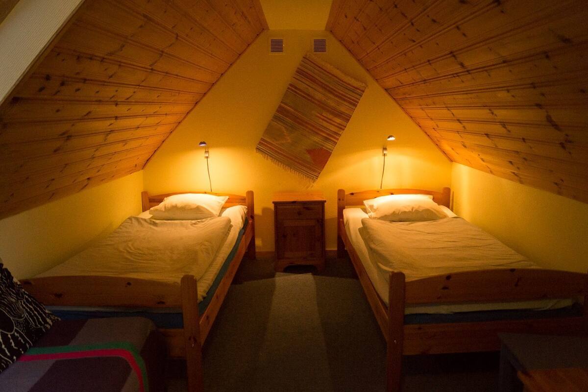 Un pequeño dormitorio en el ático con dos camas de madera, una mesita de noche y techo inclinado.