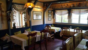 L’intérieur de ce restaurant est chaleureux, avec des tables et des bancs en bois, des tableaux encadrés aux murs et une fenêtre agrémentée de rideaux.