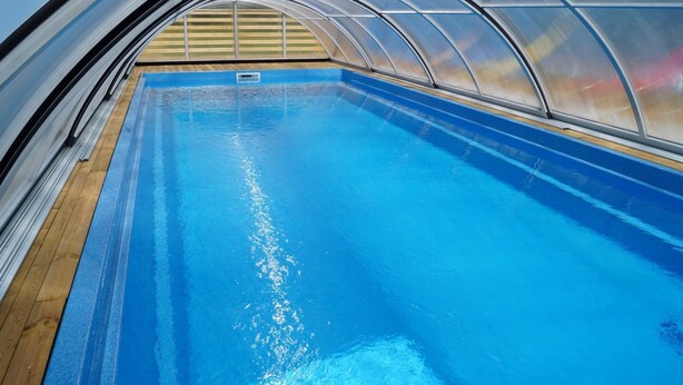 Une piscine intérieure dotée d’une terrasse en bois et d’un toit en verre.