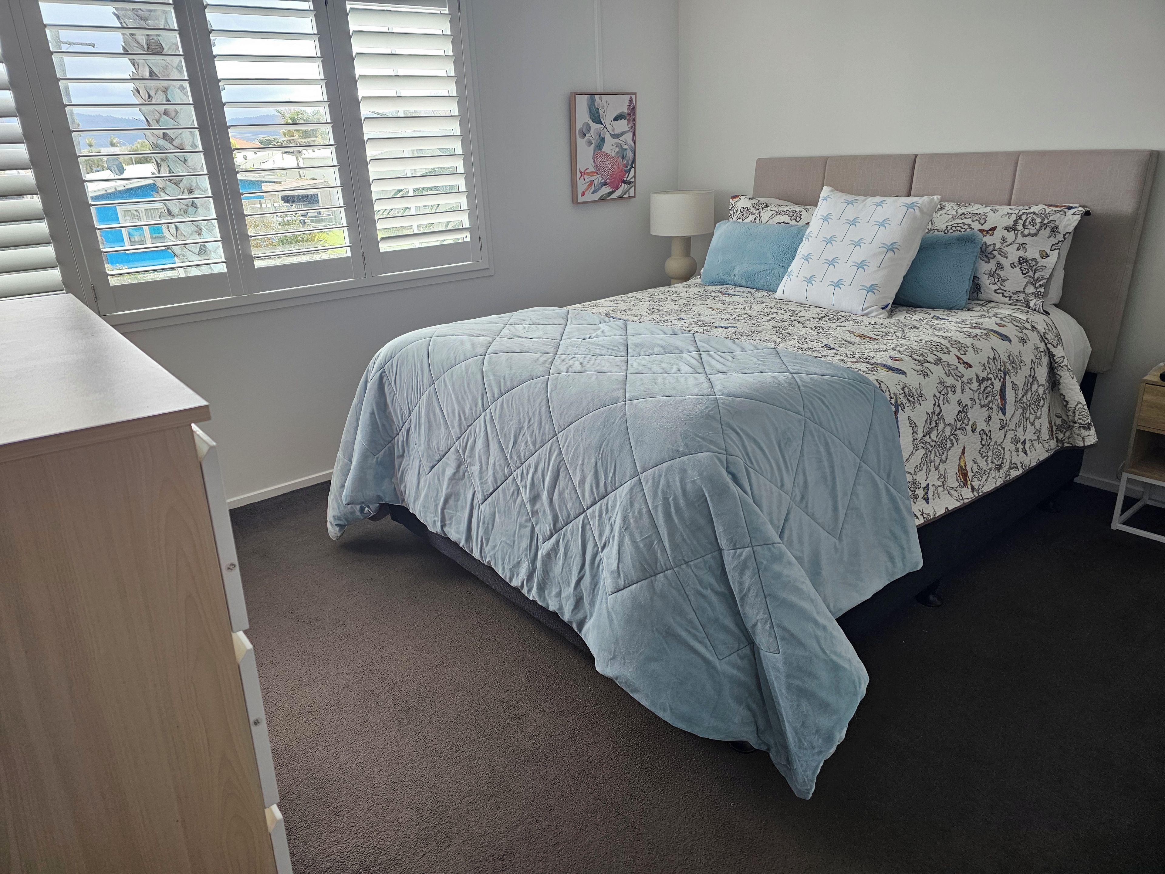 A bedroom with a bed, a bedside table, a lamp, and a window with blinds.