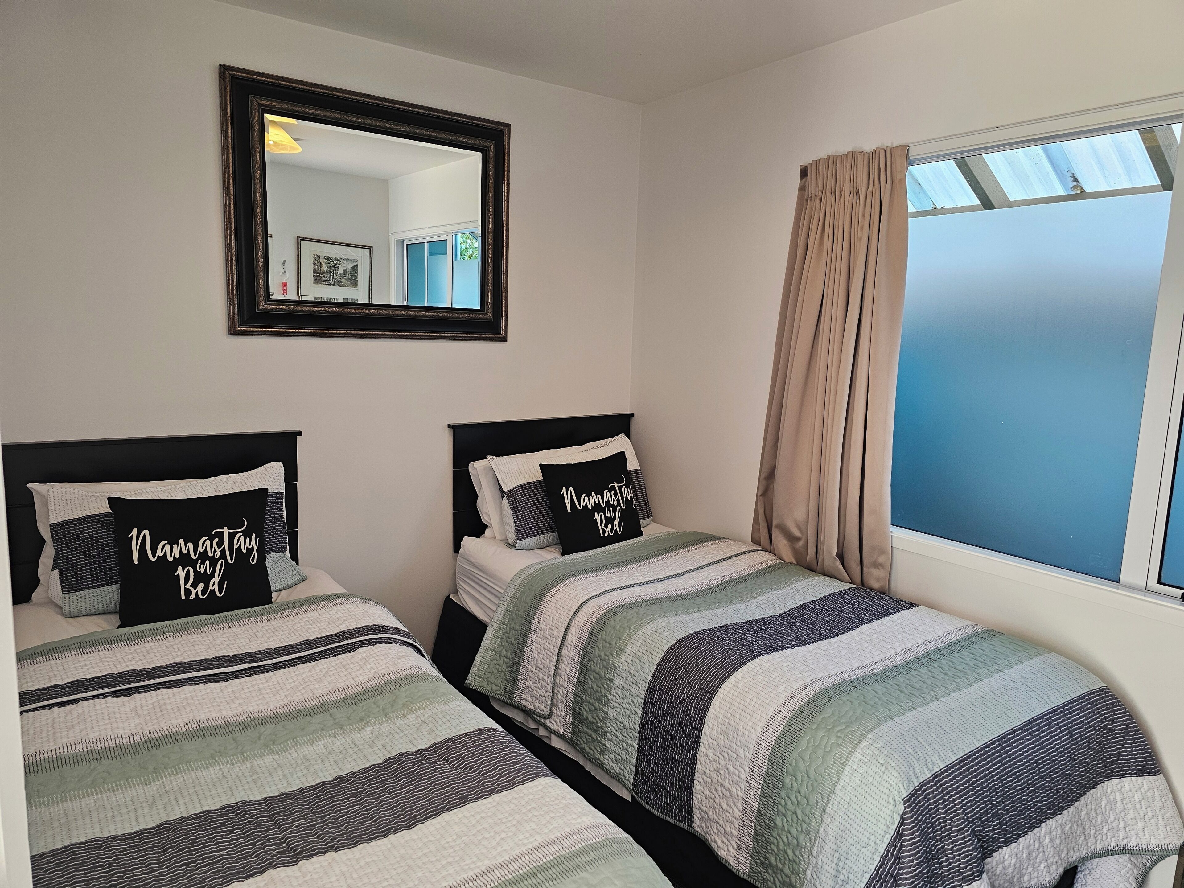 A bedroom with two beds, a mirror, and a window with curtains.