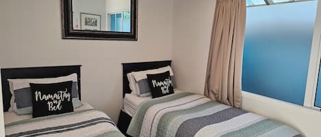 A bedroom with two beds, a mirror, and a window with curtains.