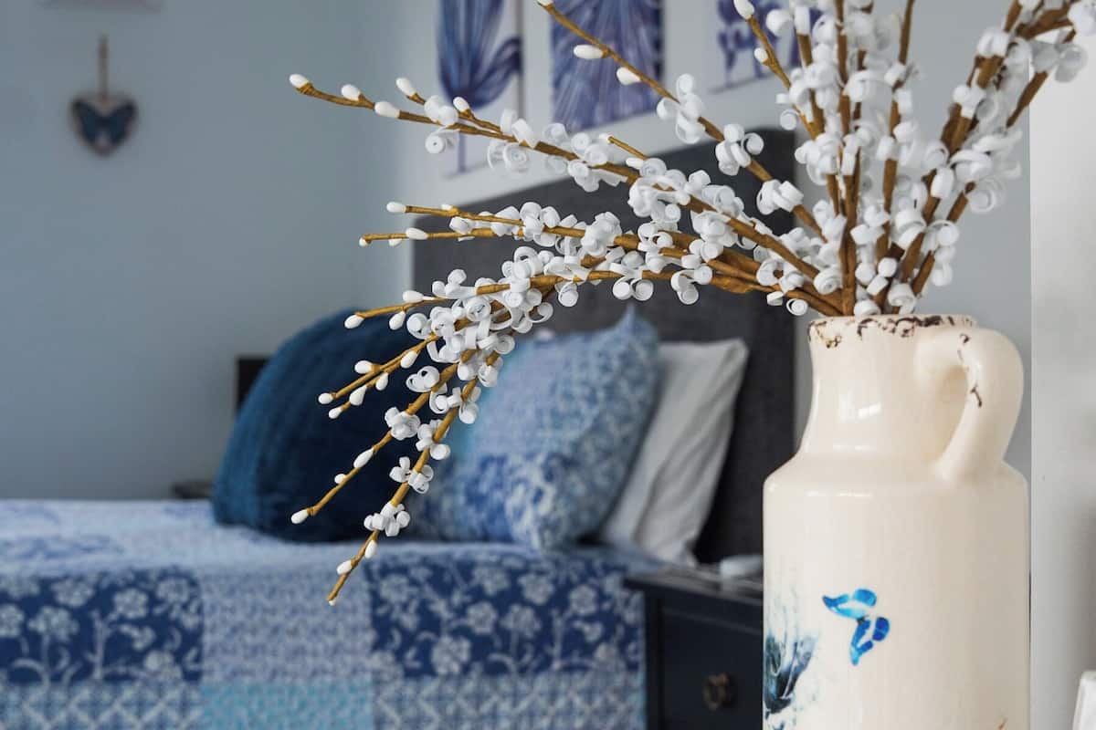 Une pièce avec un lit, un vase décoré de branches et un mur orné d’œuvres d’art.