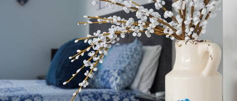 Una habitación con una cama, un jarrón con ramas y una pared decorada con obras de arte.