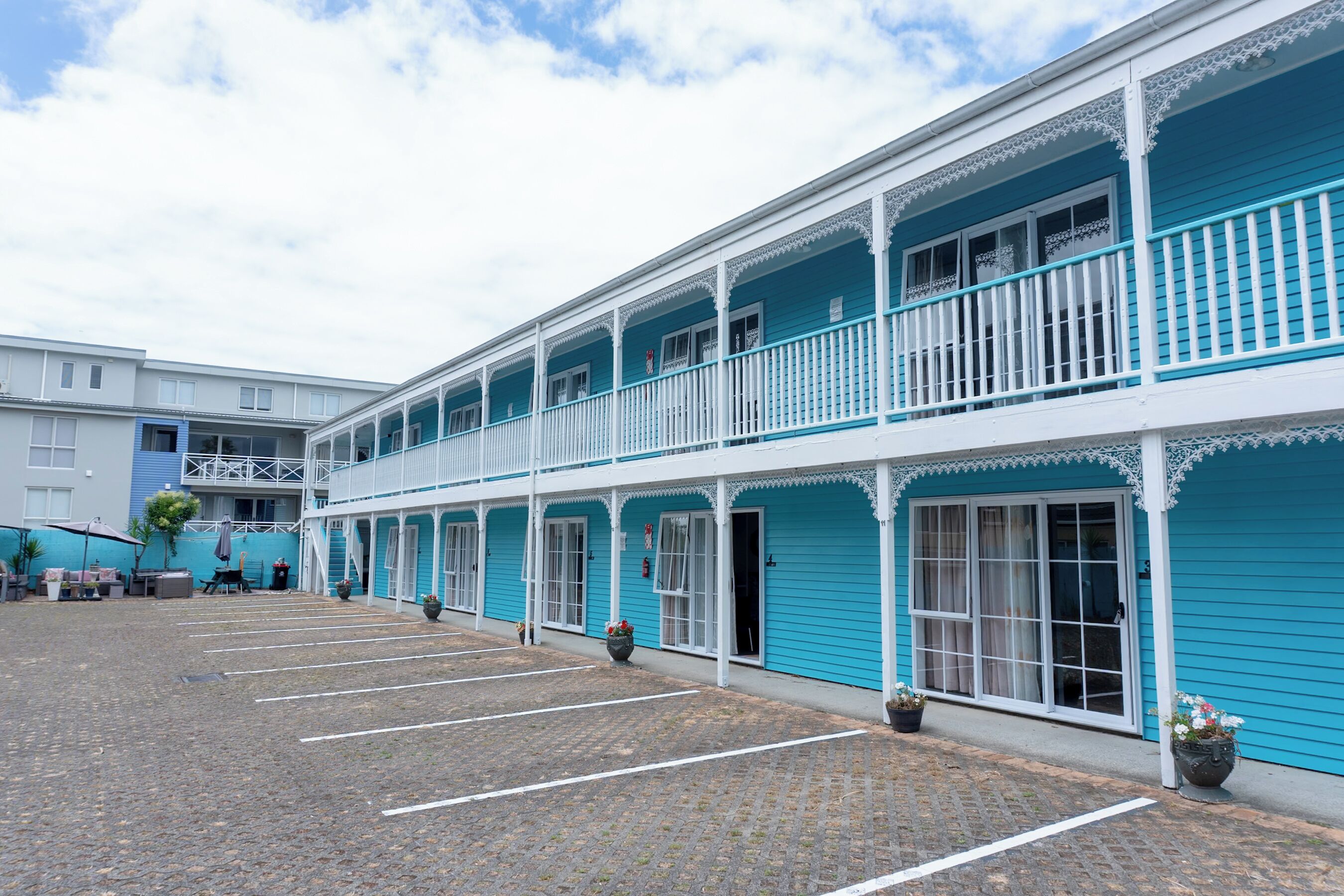A two-story building with a blue exterior, white railings, and a paved courtyard.