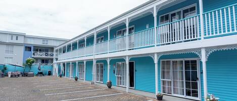 A two-story building with a blue exterior, white railings, and a paved courtyard.