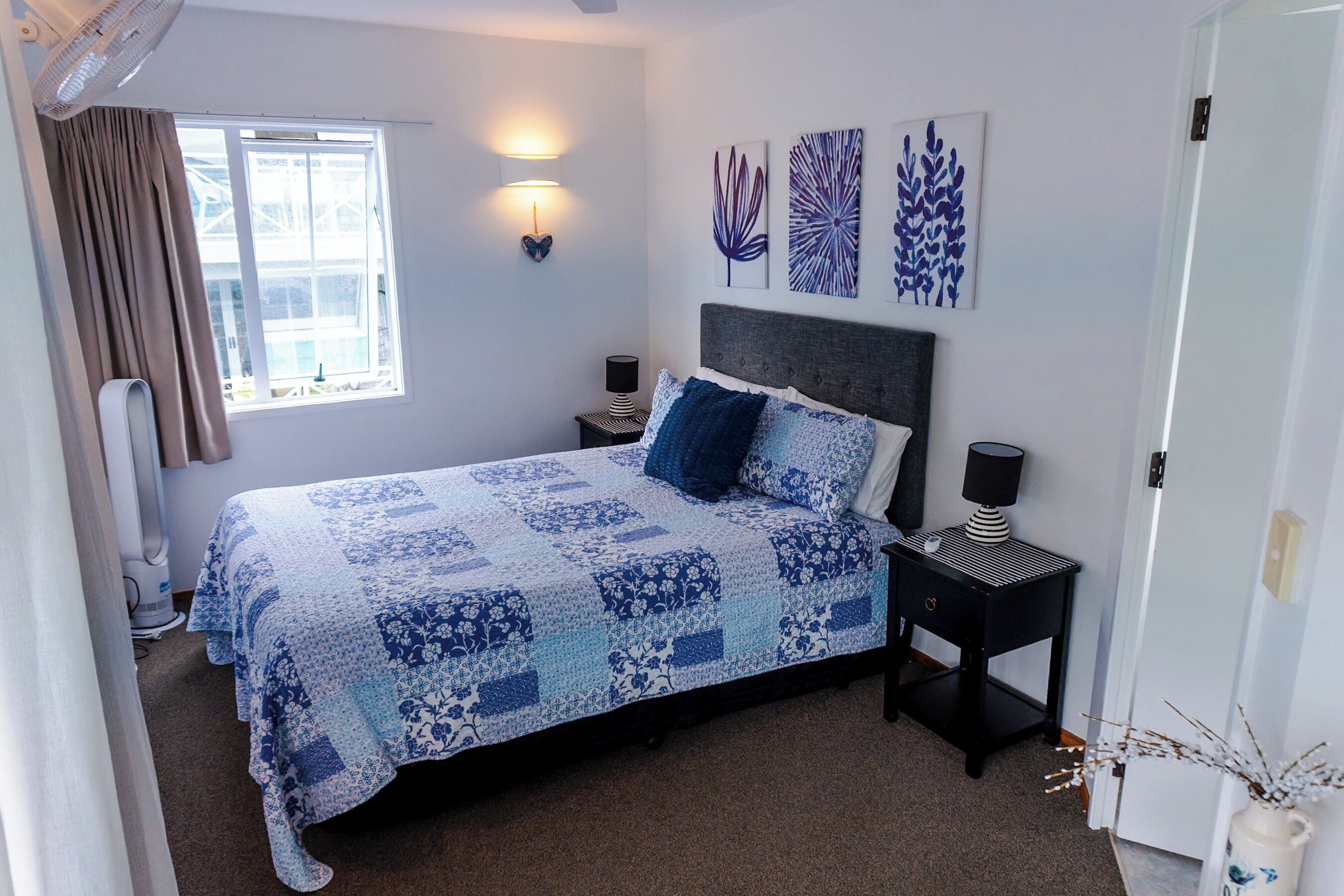 A bedroom with a bed, bedside tables, wall art, a window, and a radiator.